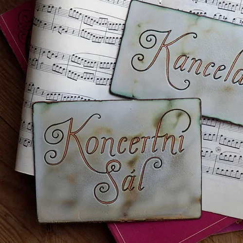 Zwei Emaille-Schilder mit den Aufschriften „Kancelář“ und „Koncertní sál“, vollständig auf Notenblättern liegend.