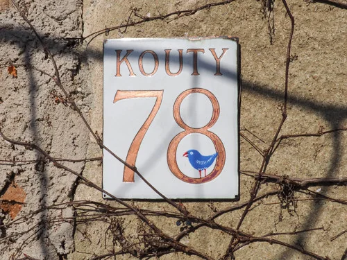 Vollständiges Schild „Kouty 78“ an einer Steinmauer mit kahlen Ranken.