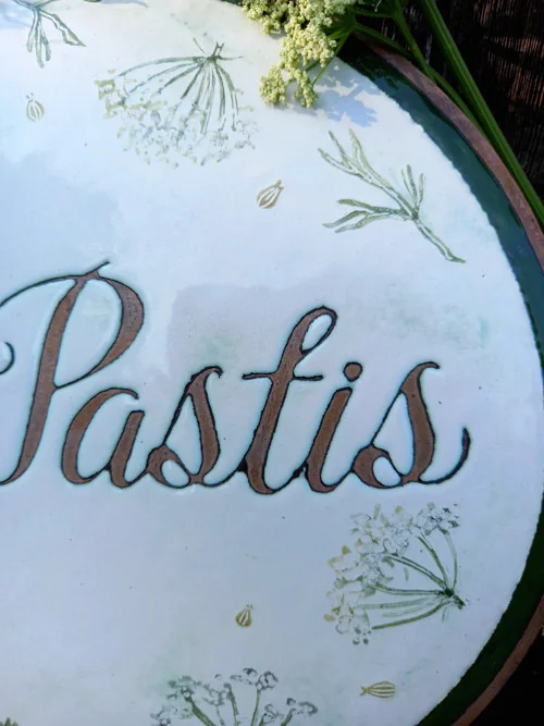 Nahaufnahme des Schriftzugs „Pastis“ und der botanischen Zeichnung auf dem ovalen Schild.